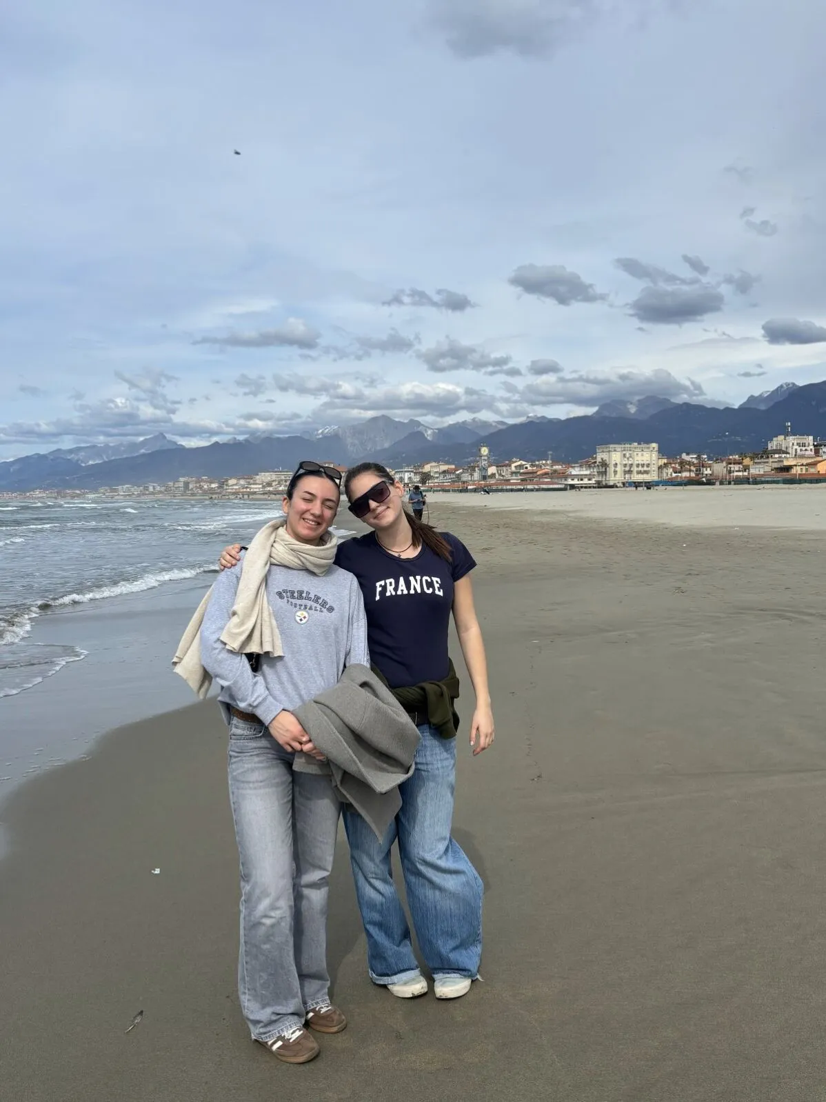 Zwei Schülerinnen an einem Sandstrand am Meer, im Hintergrund Berge